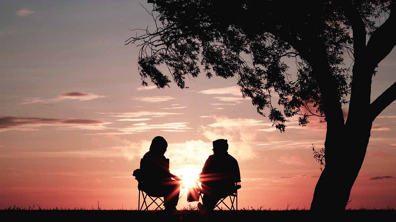 two people sitting in front of a sunset